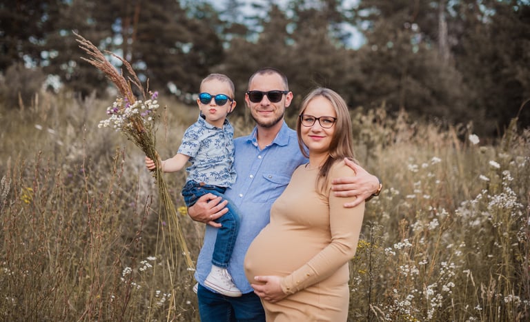 Laukimo fotosesija su šeima, nėštukė laiko savo pilvuka, šalia vaikas ir vyras
